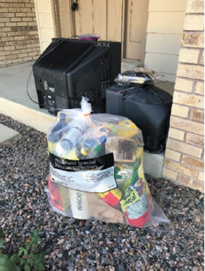 A trash bag full of hazardous waste and old televisions on a curb.