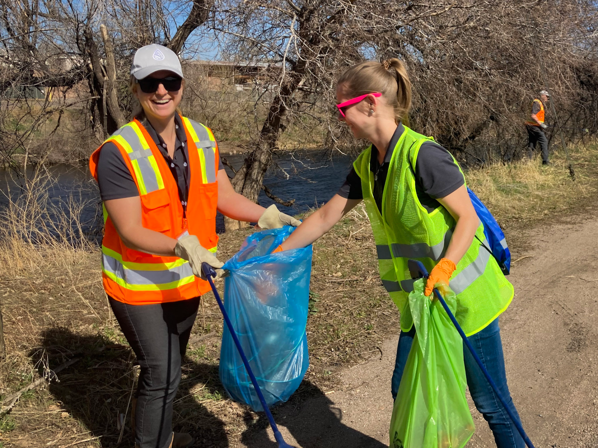 Two people in vests cleaning up trash from the riverfront. 